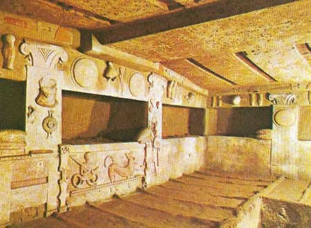 The Tomb of the Reliefs at Cerveteri is carved in the solid rock to represent a room in a house, with raftered ceiling supported on pillars, proto-Ionic capitals and bed niches in the walls.